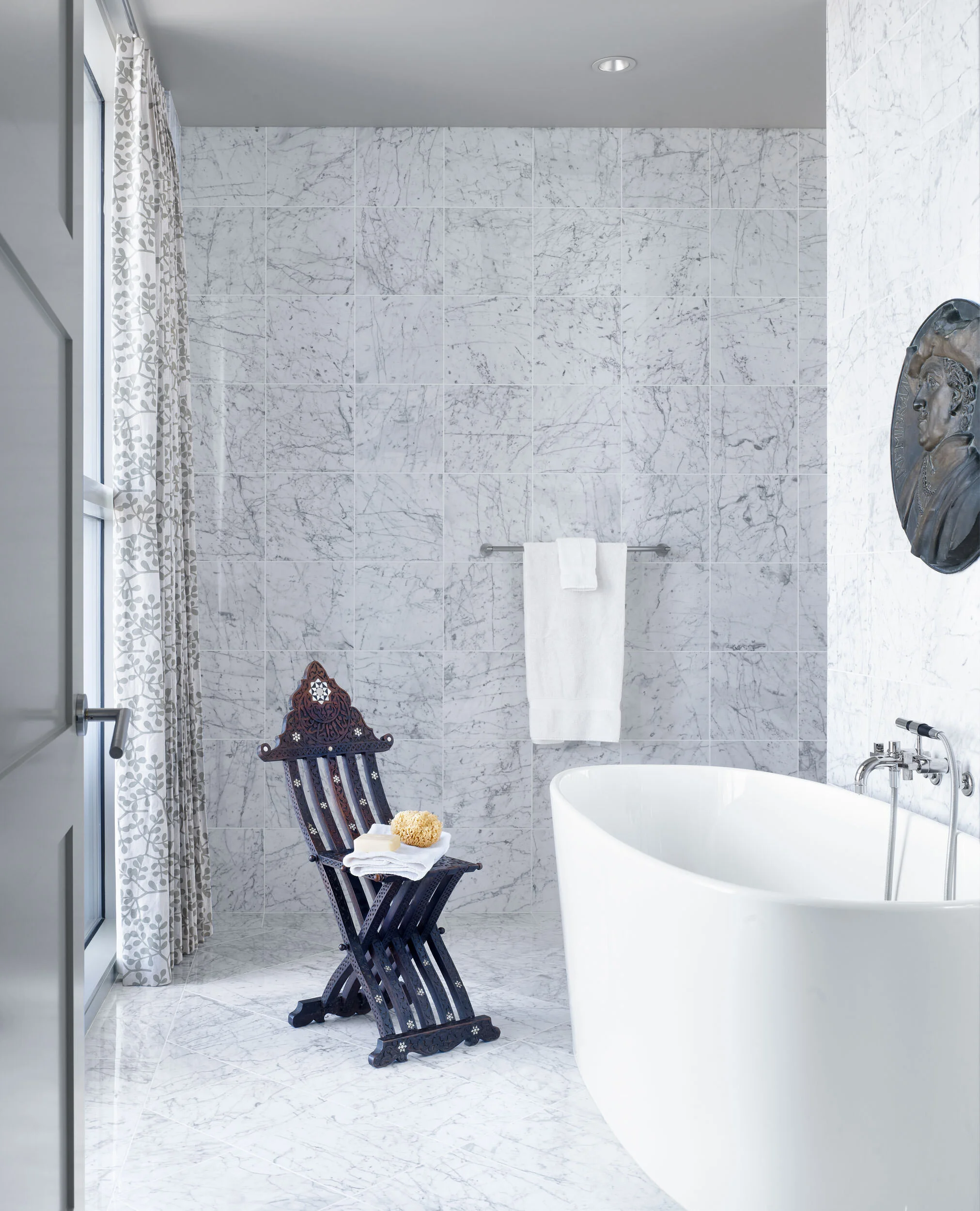  White marble bathroom with antique chair and freestanding tub at the Four Seasons Penthouse, designed by Mark Cravotta. 