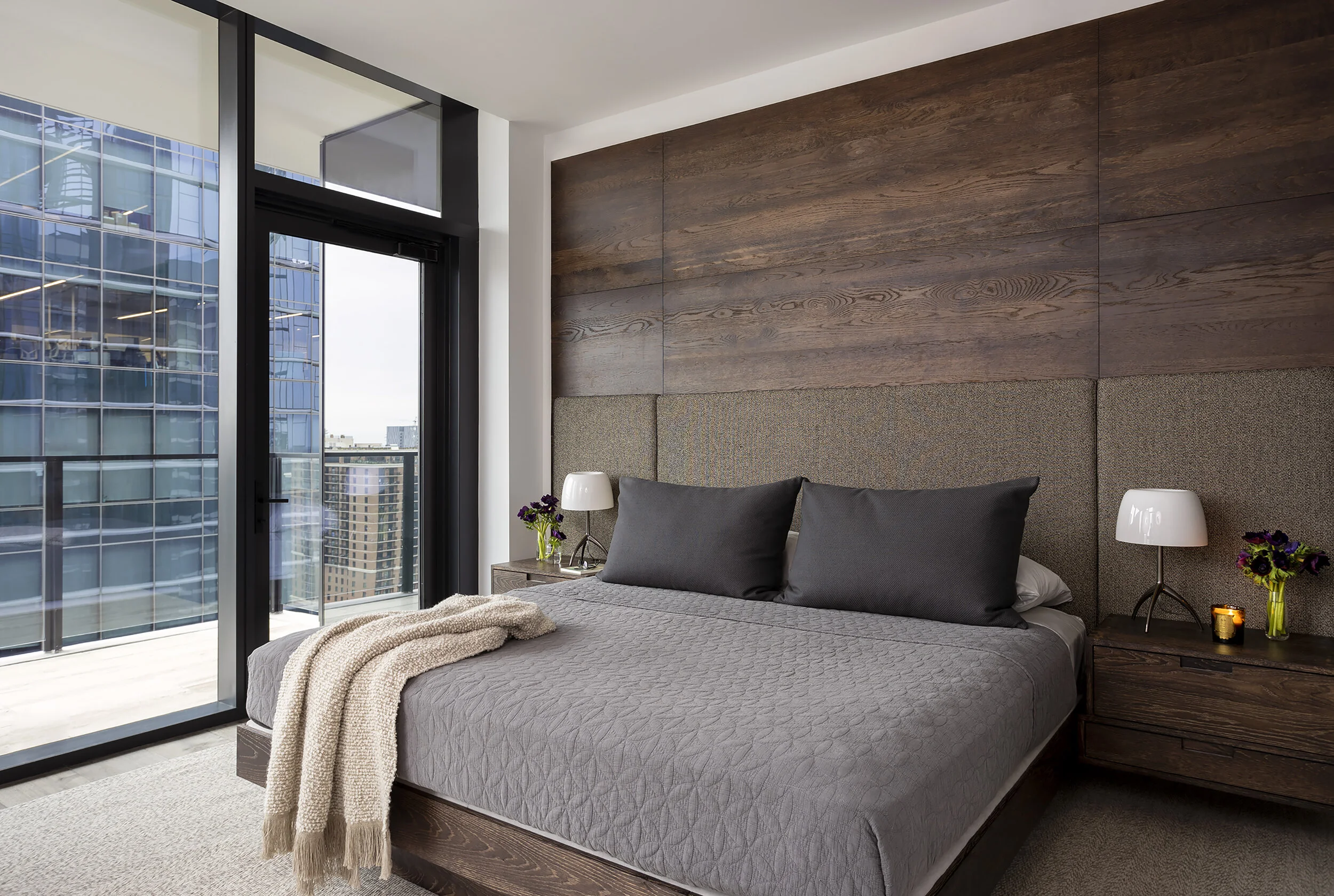  Primary bedroom with custom dark oak bed, wall paneling, and built-in nightstands at the Proper Penthouse by Cravotta Interiors. 