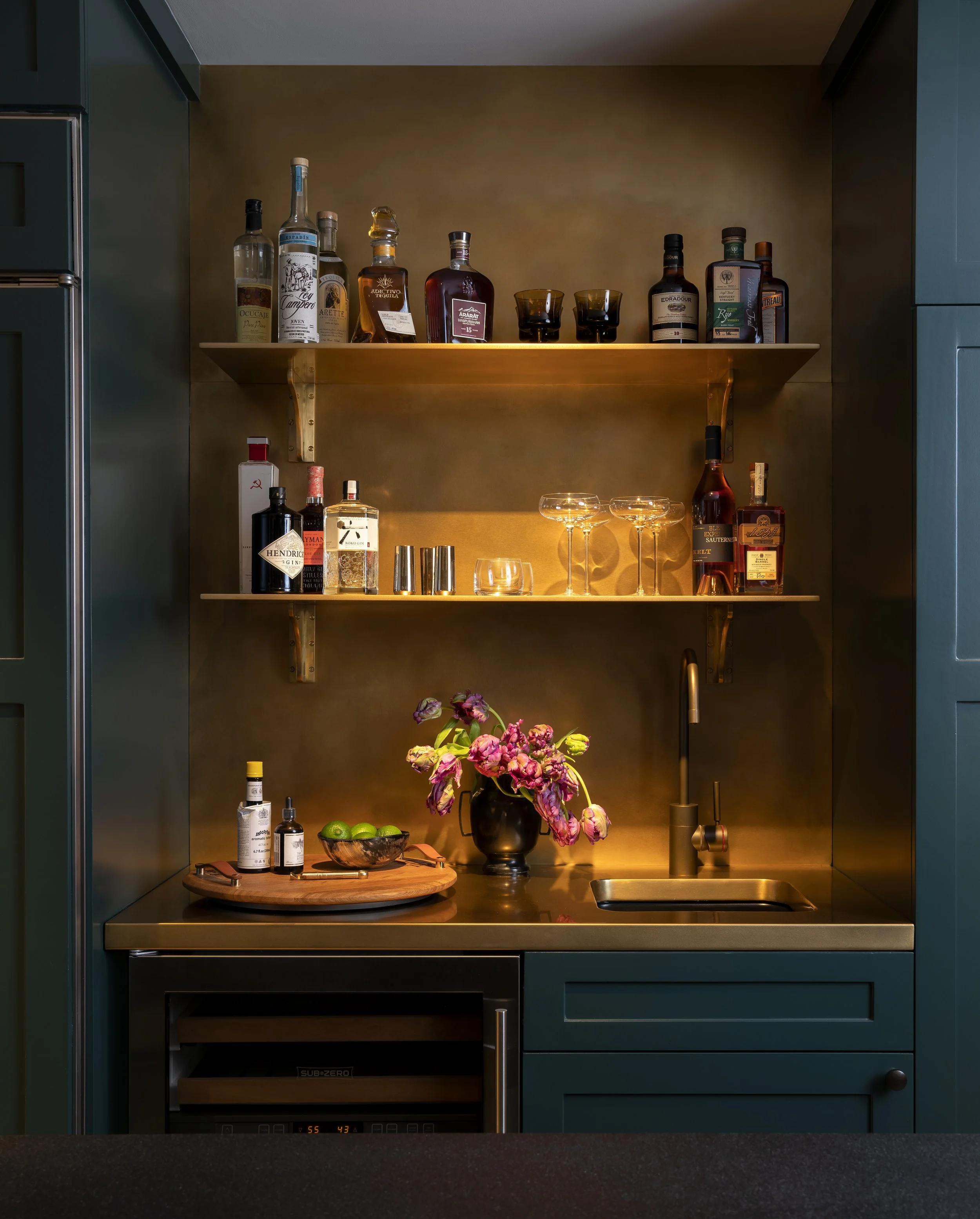  Dark, moody bar detail with green cabinetry and brass accents in the Boulevard Oaks kitchen, designed by Mark Cravotta. 