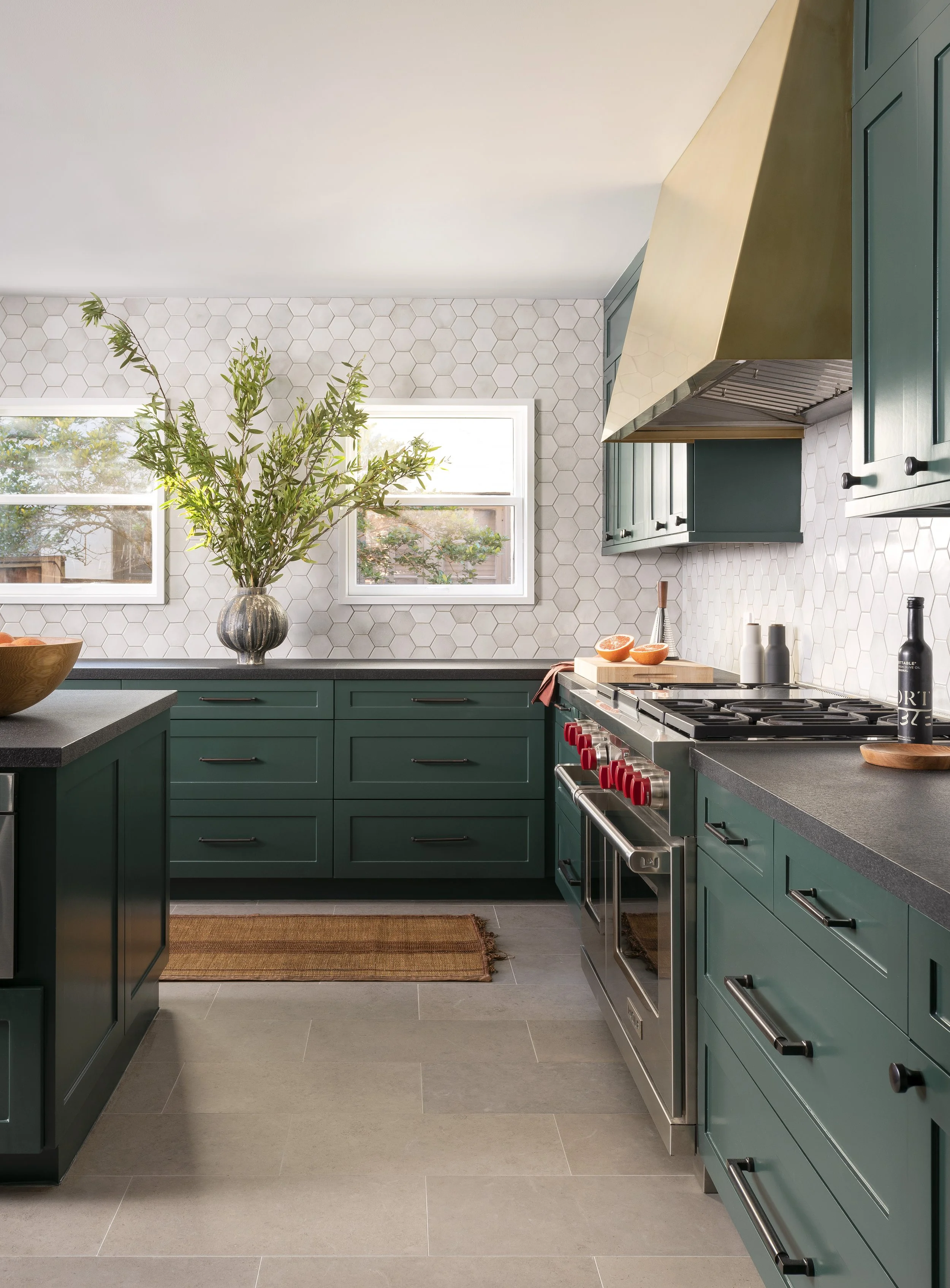  Kitchen with dark green cabinets, brass vent hood, and handmade hex tile backsplash at Boulevard Oaks by Cravotta Interiors. 